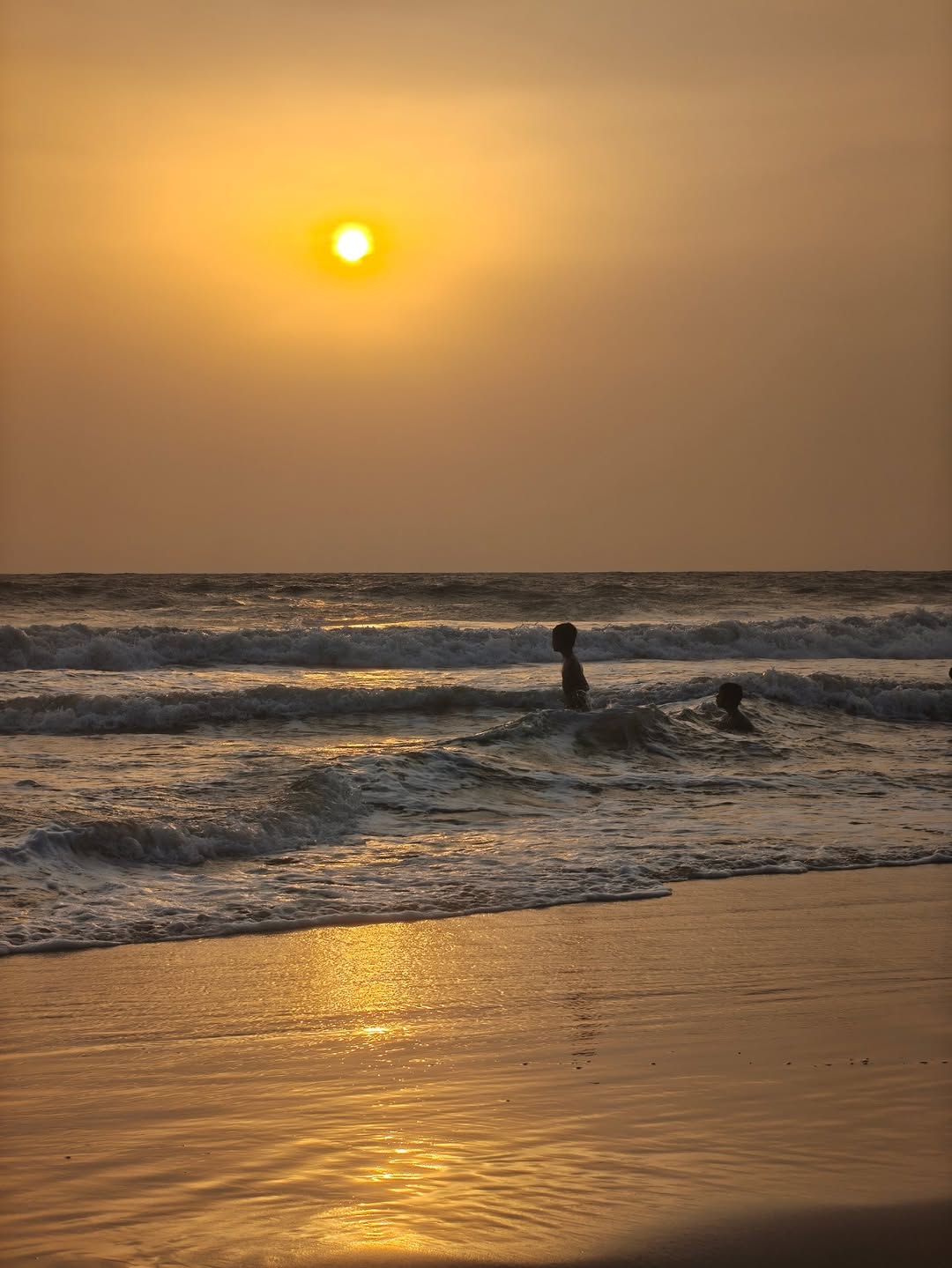 Swimmers in the surf under a low sun