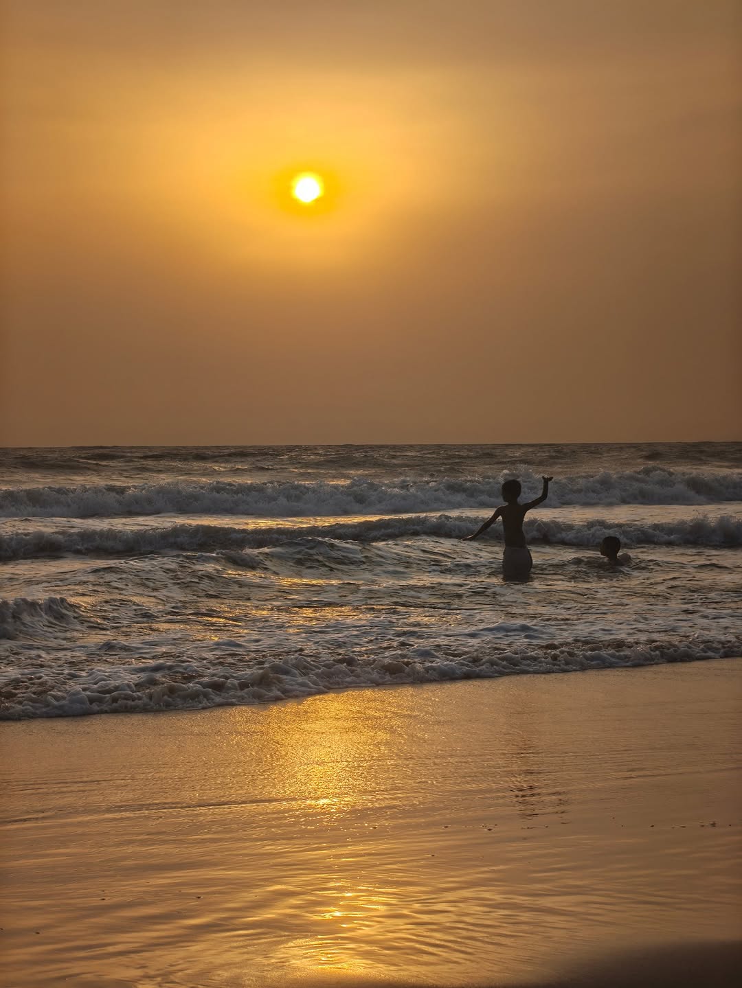 A boy waving from the waves at sunset