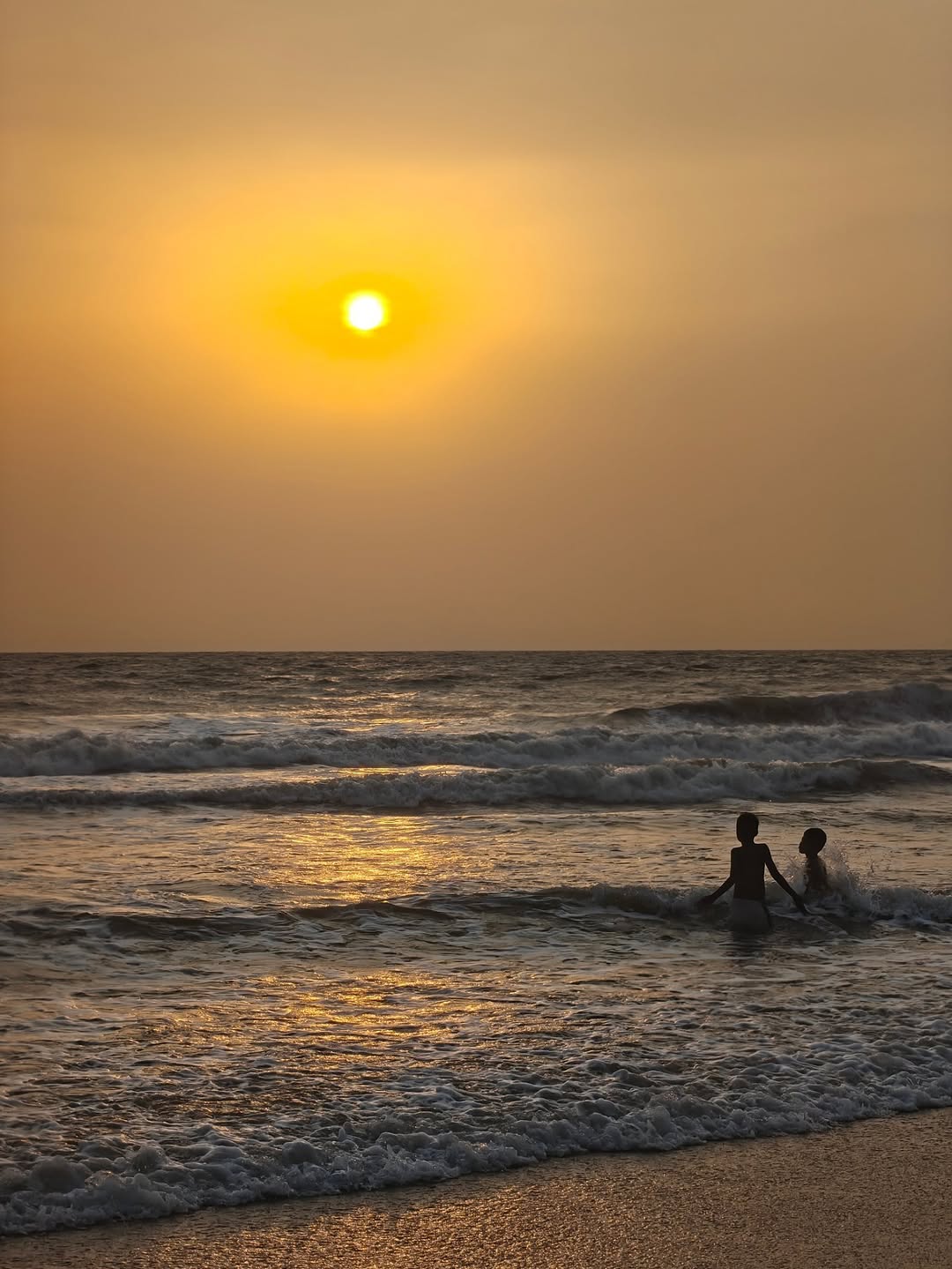 Two figures wading, sun low over the sea